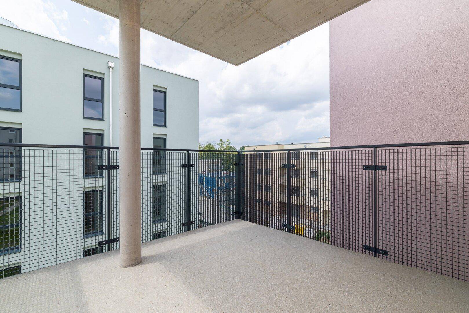 Eckbalkon mit Gittergeländer und Blick auf die moderne Wohnanlage und umliegende Gebäude.