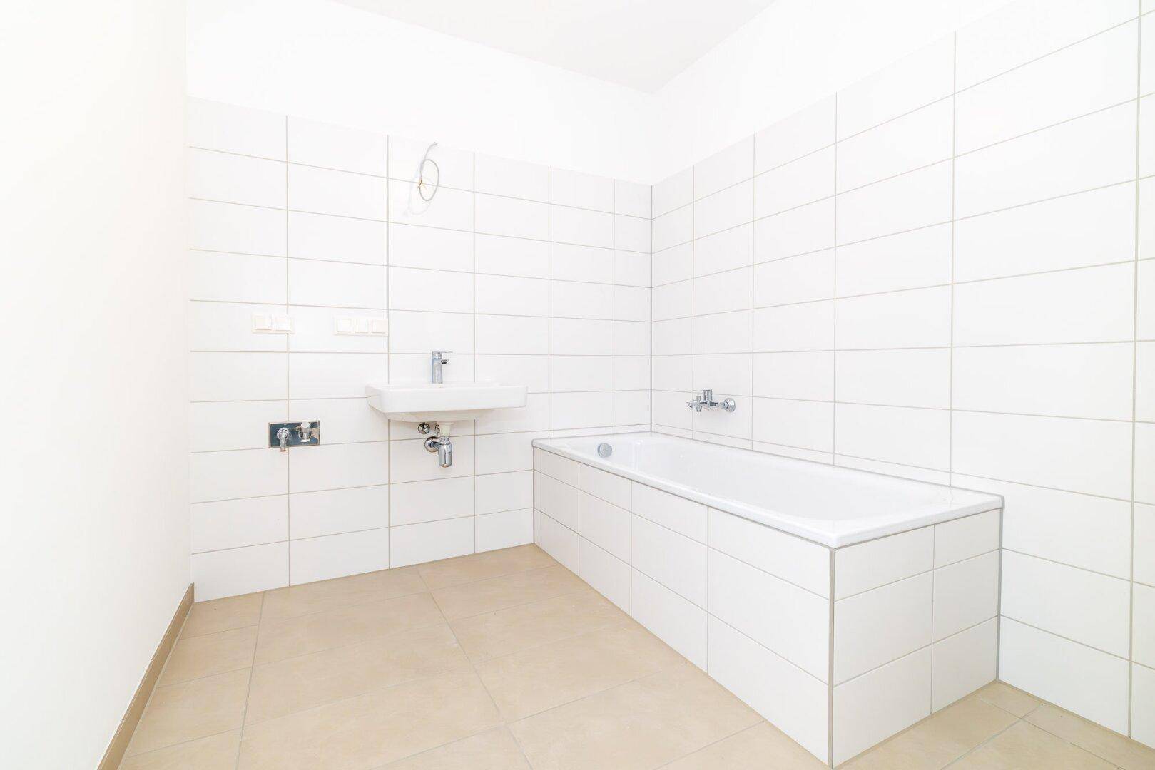 Helles Badezimmer mit Badewanne, Waschbecken und weißen Wandfliesen.