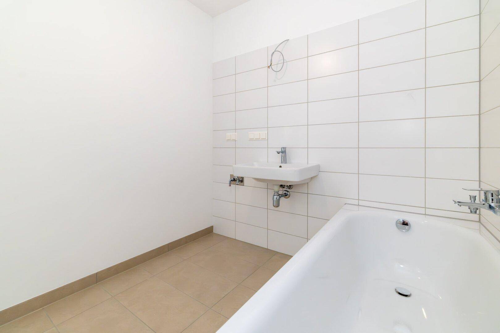 Modernes Badezimmer mit Badewanne, Waschbecken und weißen Fliesen an den Wänden.