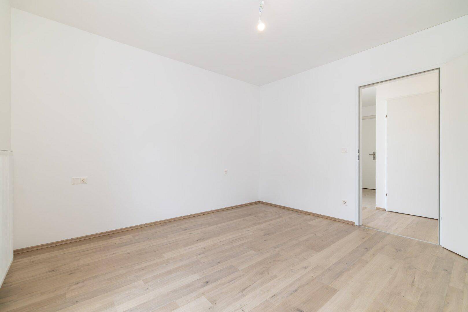 Heller Raum mit Holzboden und offener Tür, bereit zur individuellen Gestaltung.