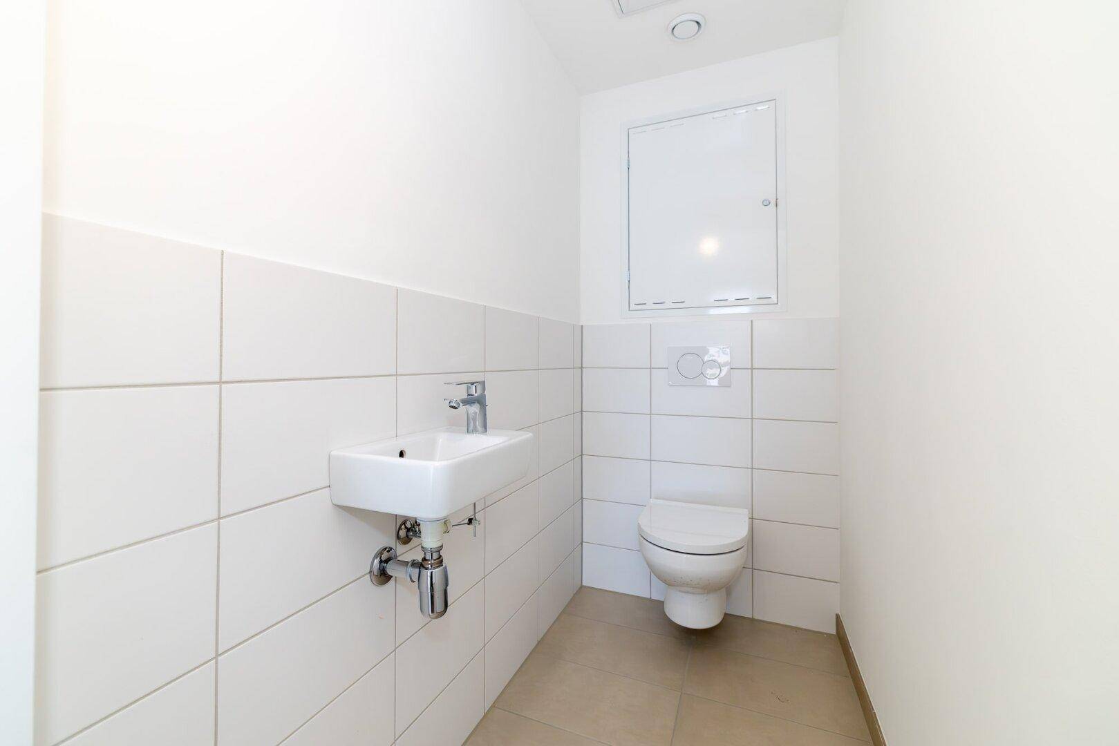 Kleines Gäste-WC mit wandhängender Toilette, Waschbecken und weißen Fliesen.