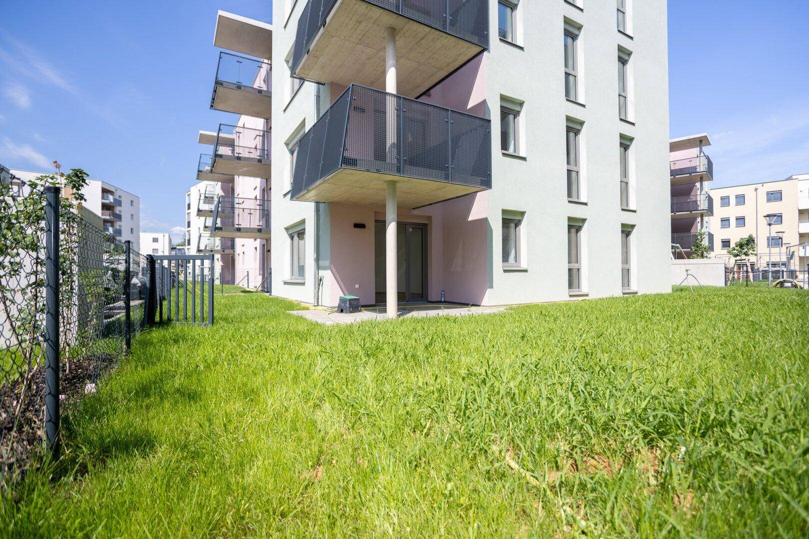 Moderne Wohnanlage mit Balkonen und einer kleinen Grünfläche vor dem Gebäude.