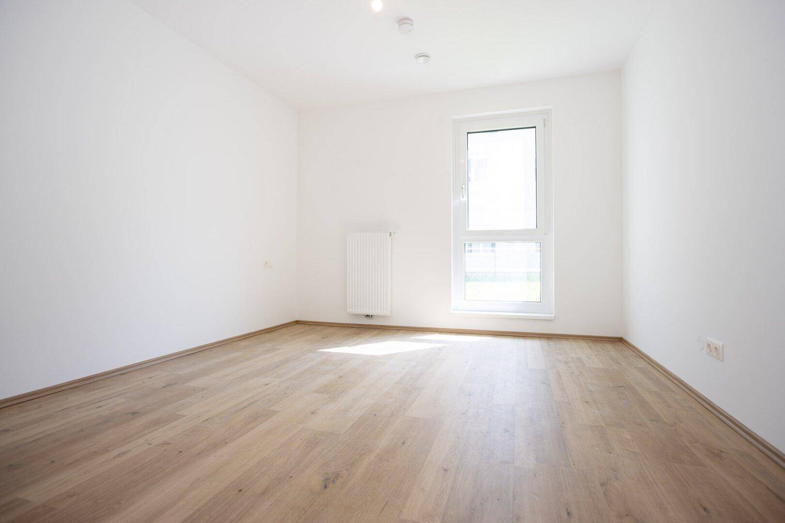 Helles Schlafzimmer mit Laminatboden, weiß gestrichenen Wänden und einem großen Fenster.