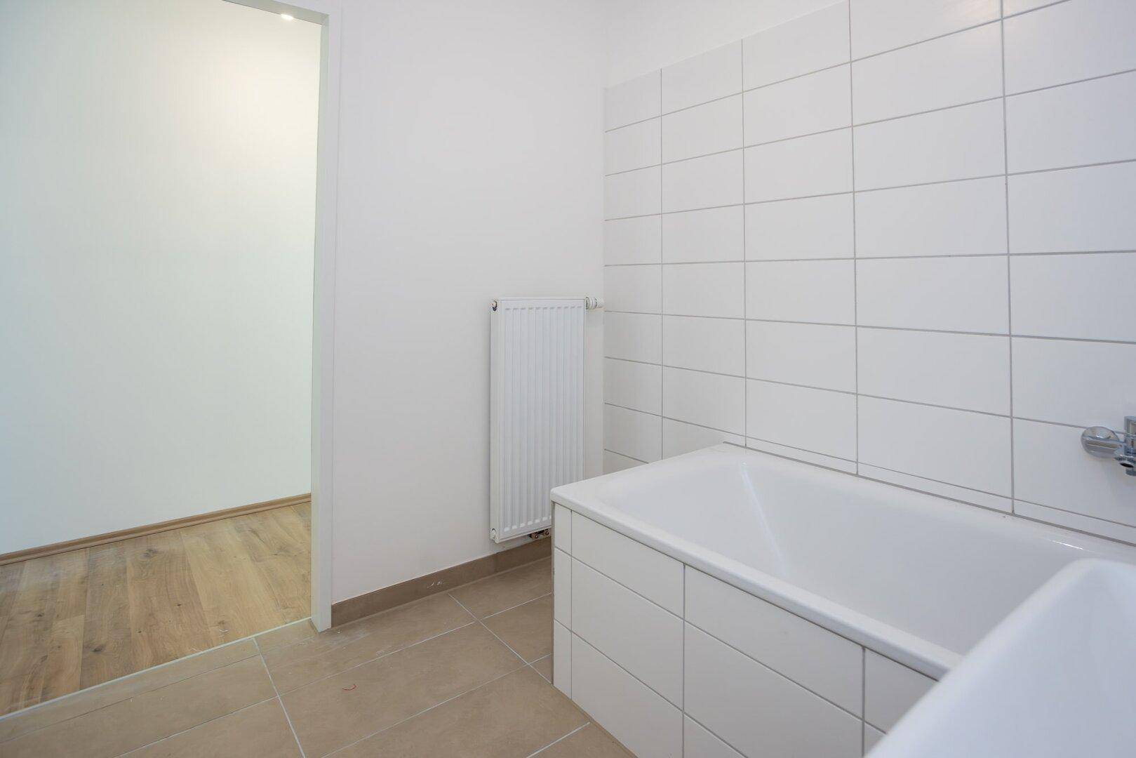 Helles Badezimmer mit Badewanne, Waschbecken und weißen Wandfliesen.