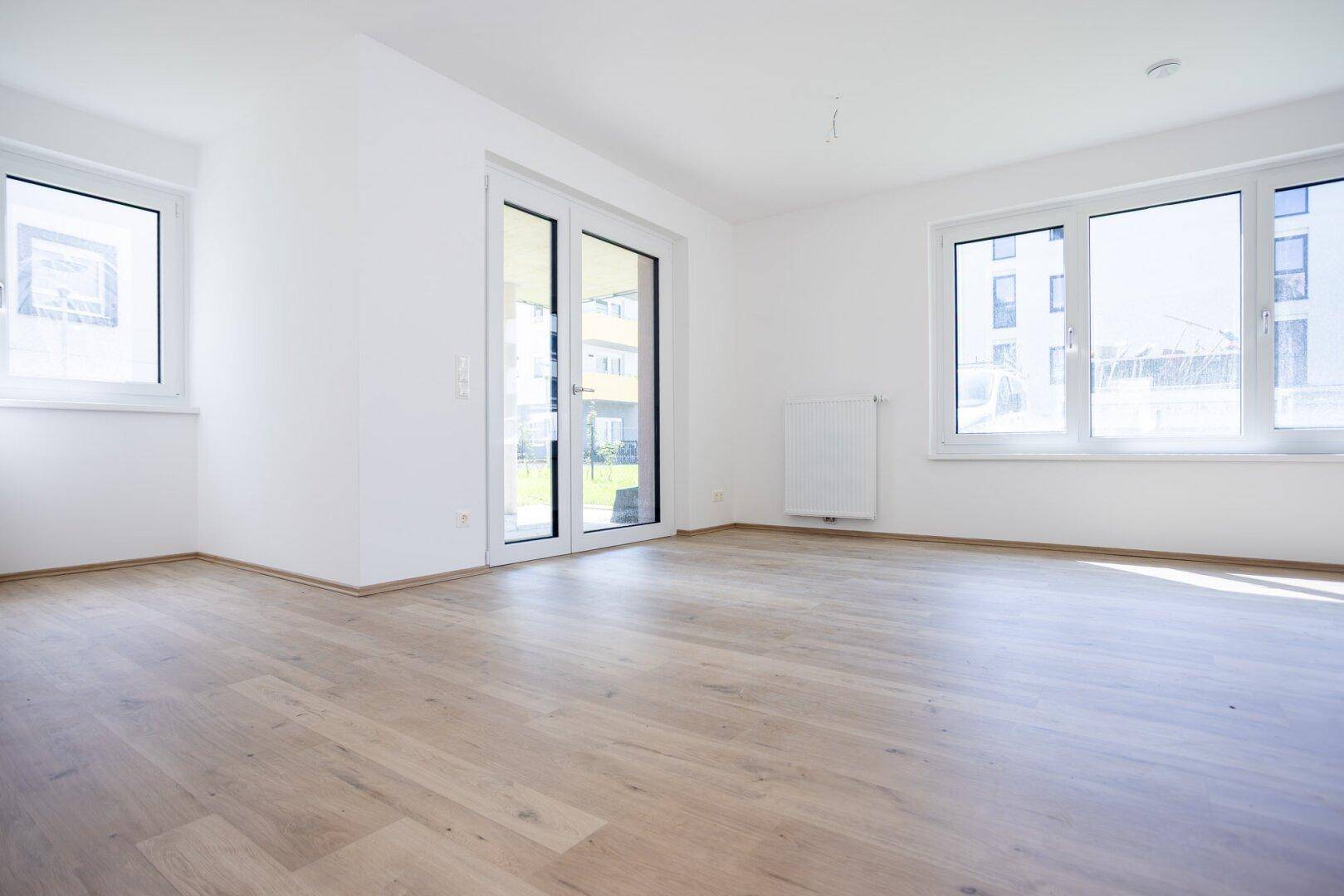 Geräumiges, helles Wohnzimmer mit Laminatboden und großen Fenstern zum Außenbereich.