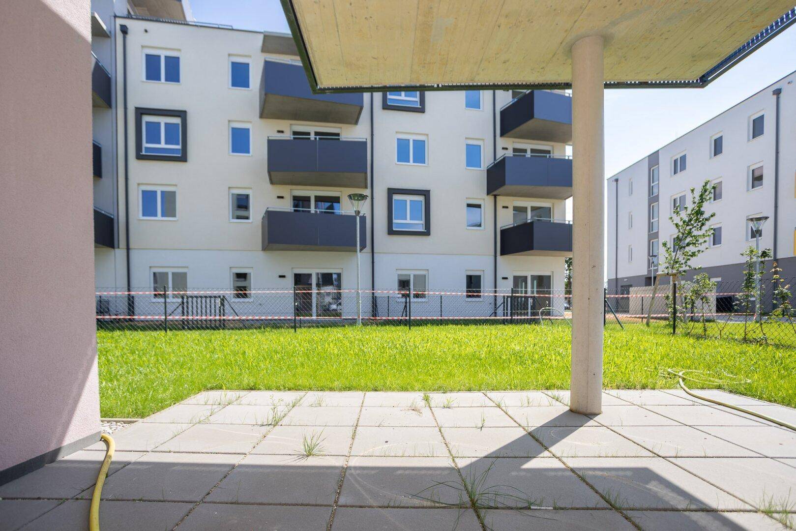 Gepflasterte Terrasse mit Blick auf die modernen Wohngebäude und eine Grünfläche.