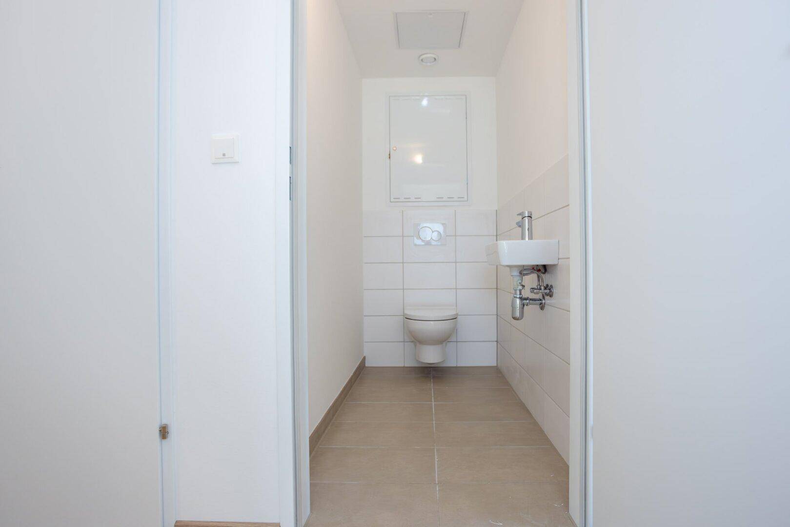Separates Gäste-WC mit Wand-WC, kleinem Waschbecken und weißen Fliesen.