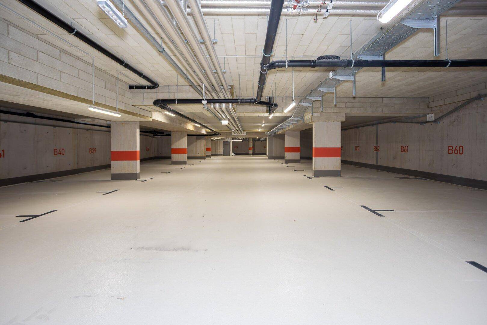 Geräumige Tiefgarage mit vielen Parkplätzen und sichtbaren Installationen an der Decke.