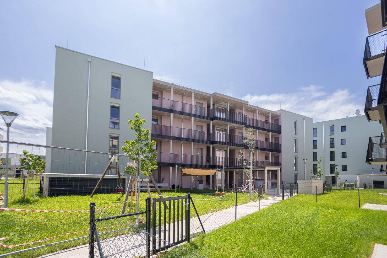 Moderne Wohngebäude mit Balkonen und einer weitläufigen Grünfläche im Neubaugebiet.