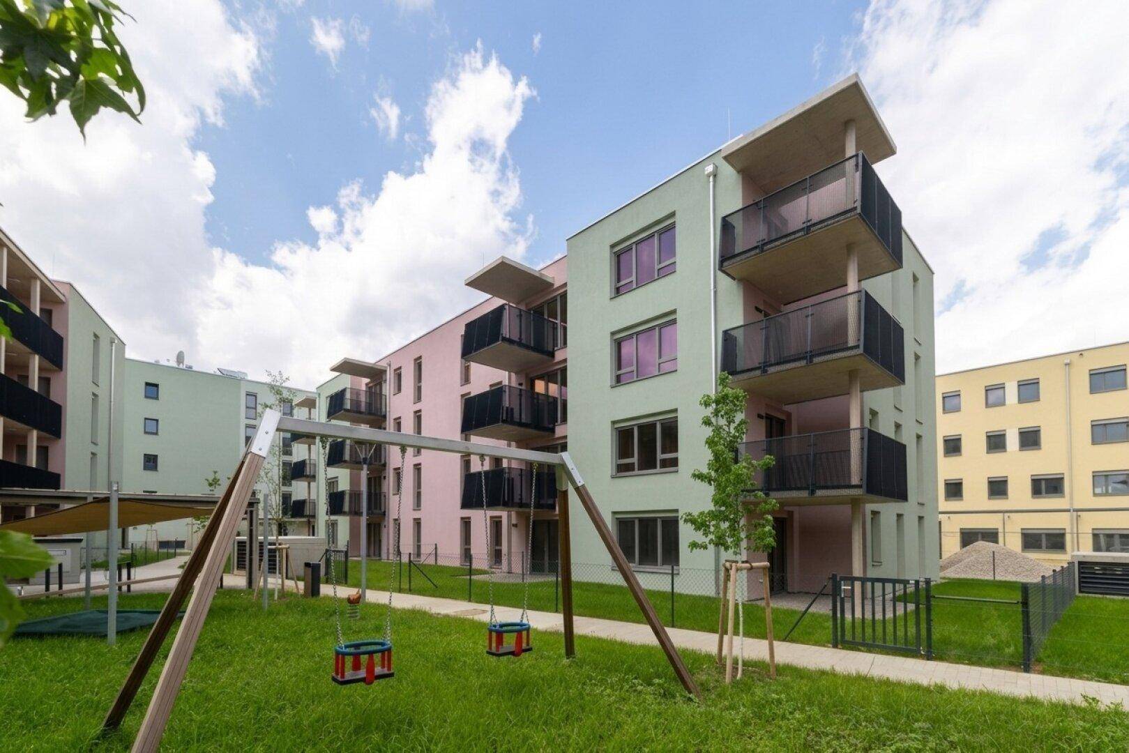 Moderne Neubauwohnungen mit farbigen Fassaden und einem gemeinschaftlichen Spielplatz im Grünen.