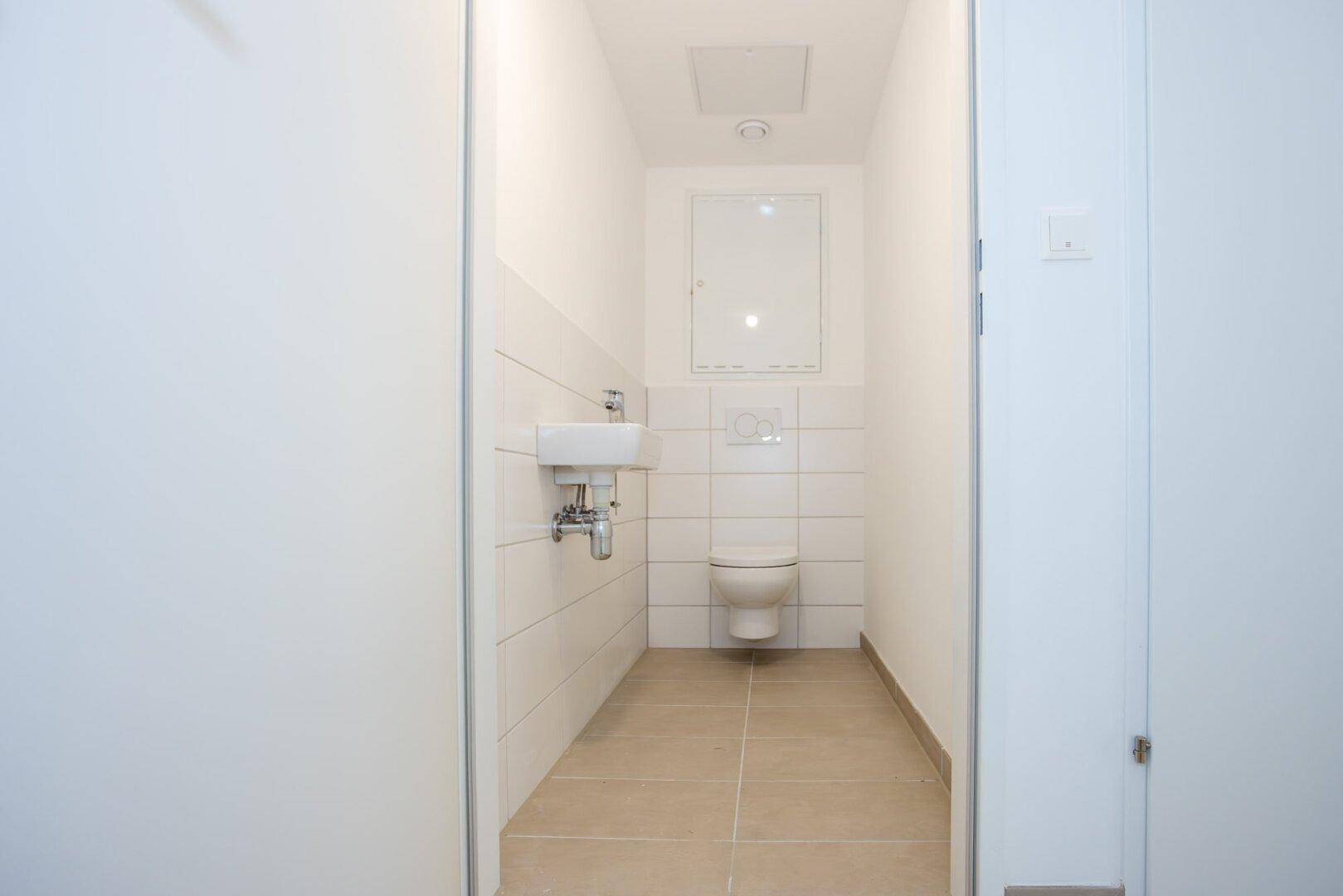 Modernes Gäste-WC mit wandhängendem WC, kleinem Waschbecken und weißen Fliesen.