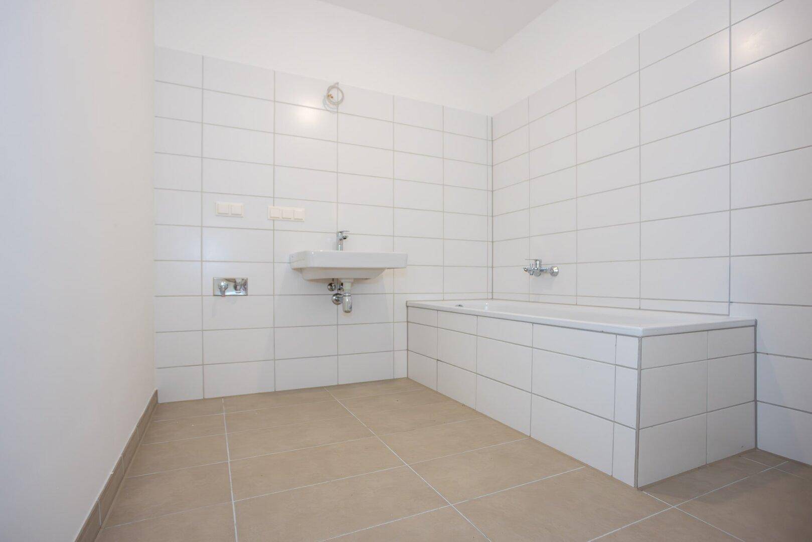 Helles Badezimmer mit Badewanne, Waschbecken und weißen Fliesen, bereit zur Nutzung.