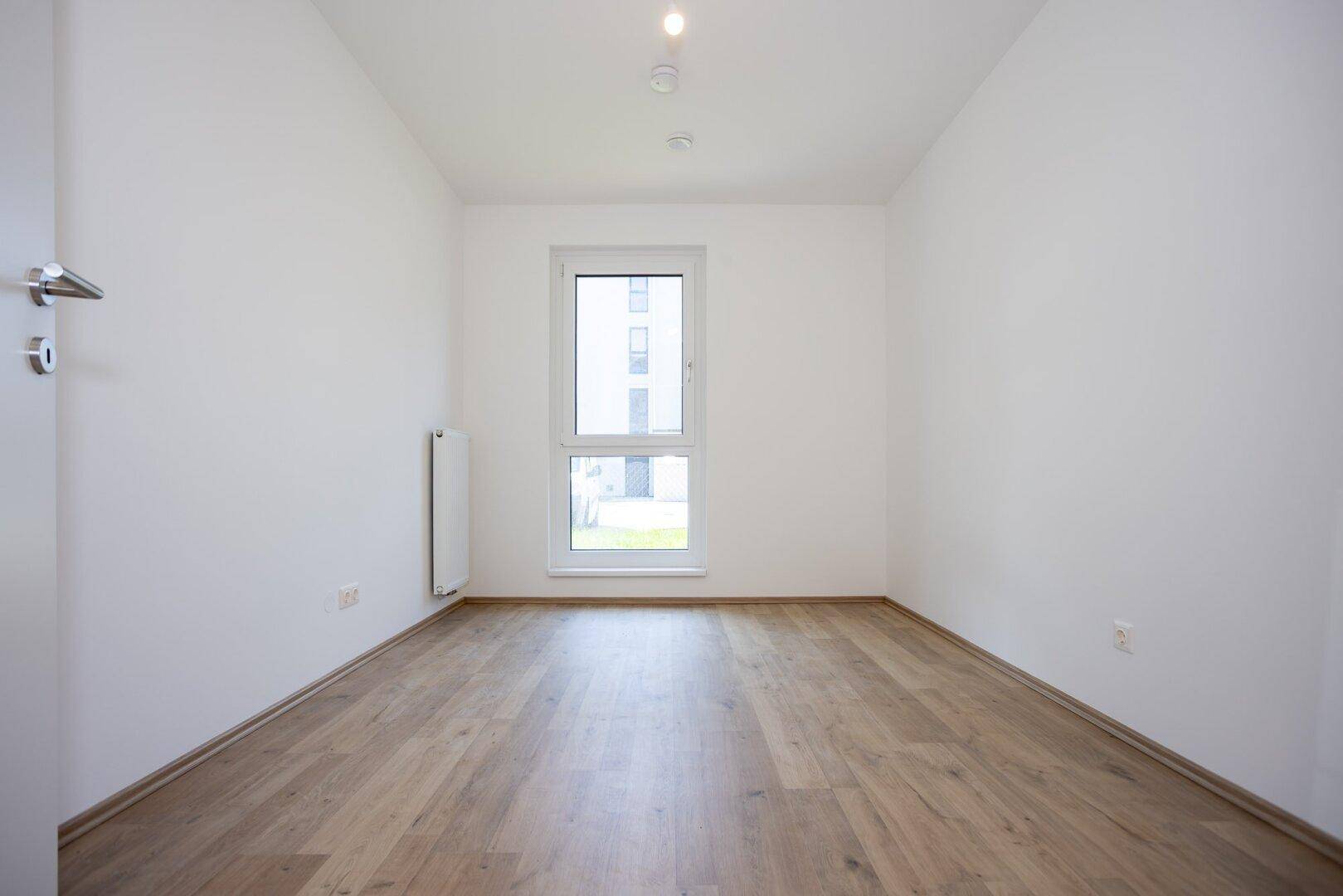 Unmöbliertes Zimmer mit Laminatboden und Fenster, bereit zum Einzug in die neue Wohnung.