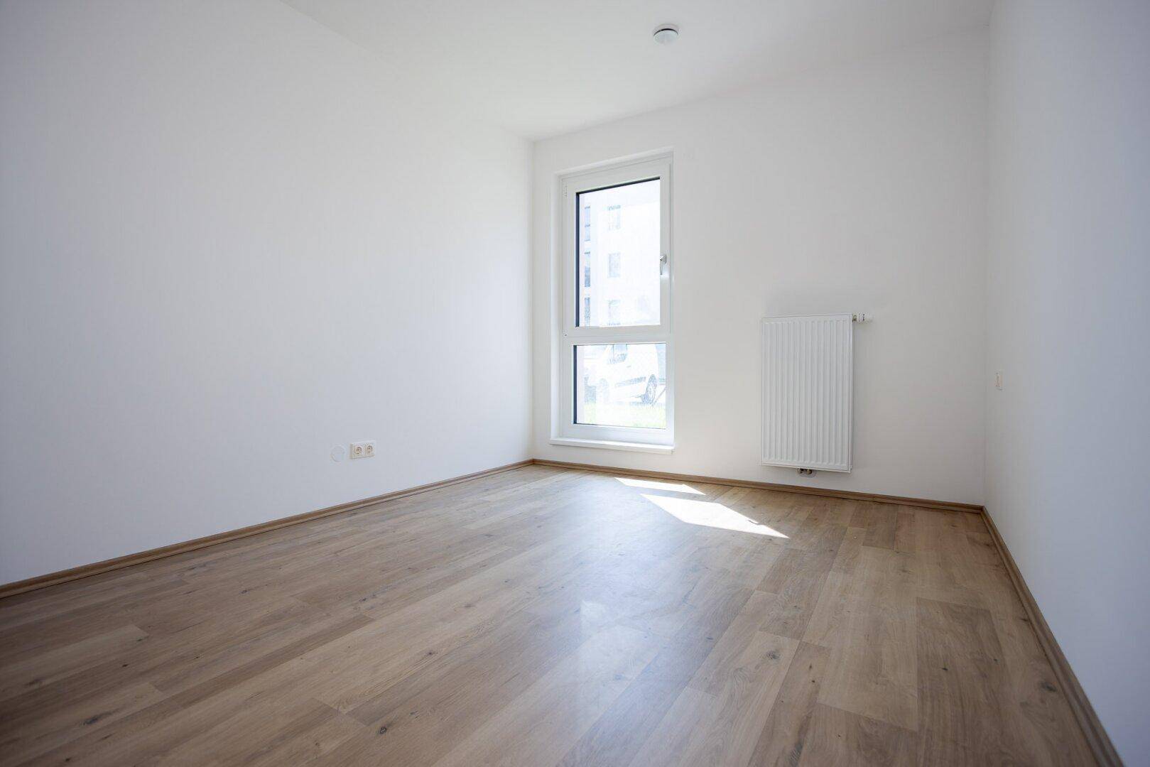 Helles Zimmer mit Laminatboden und Fenster, ideal als Schlaf- oder Arbeitszimmer in einem Neubau.