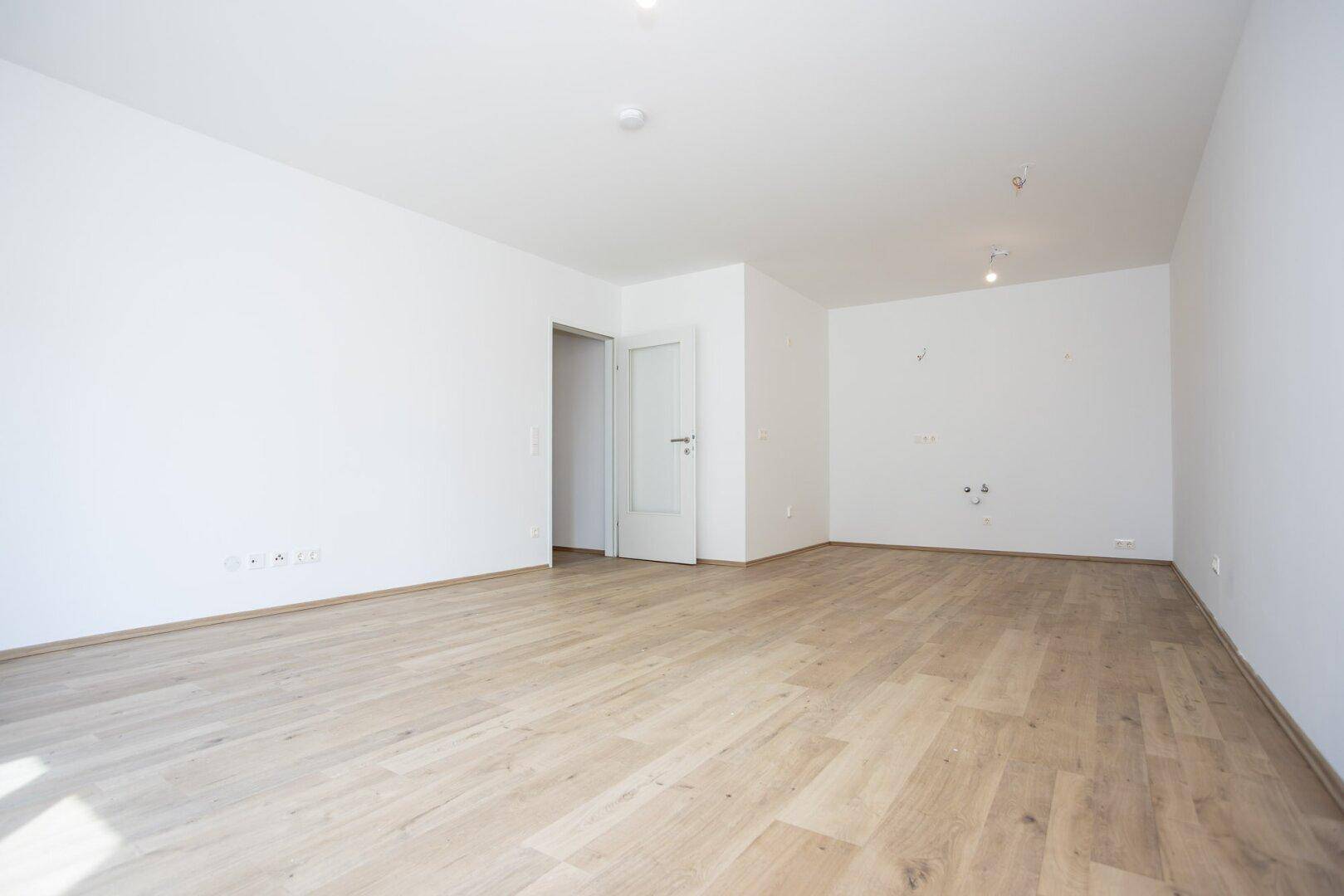 Großer offener Raum mit Laminatboden und Anschlüssen für eine zukünftige Küche.