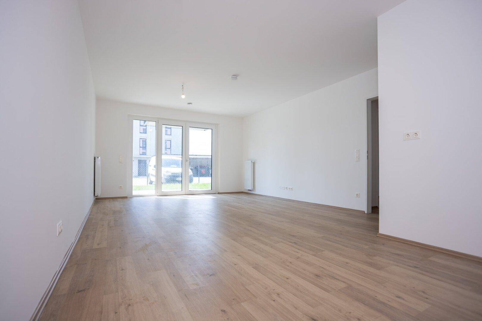 Helles Wohnzimmer mit Laminatboden und großen Fenstern, die viel Tageslicht hereinlassen.