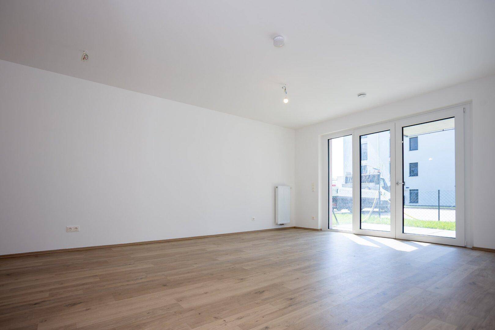 Geräumiges Wohnzimmer mit Laminatboden und großen Glastüren zum Außenbereich.