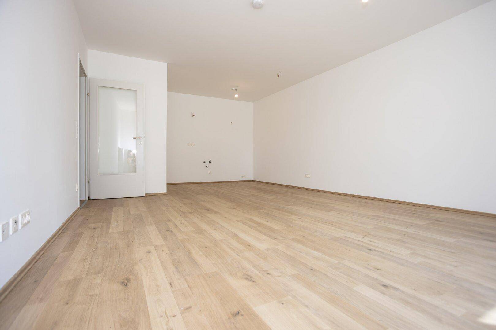 Heller, unmöblierter Raum mit Laminatboden und Tür, ideal für offenes Wohnen und Essen.