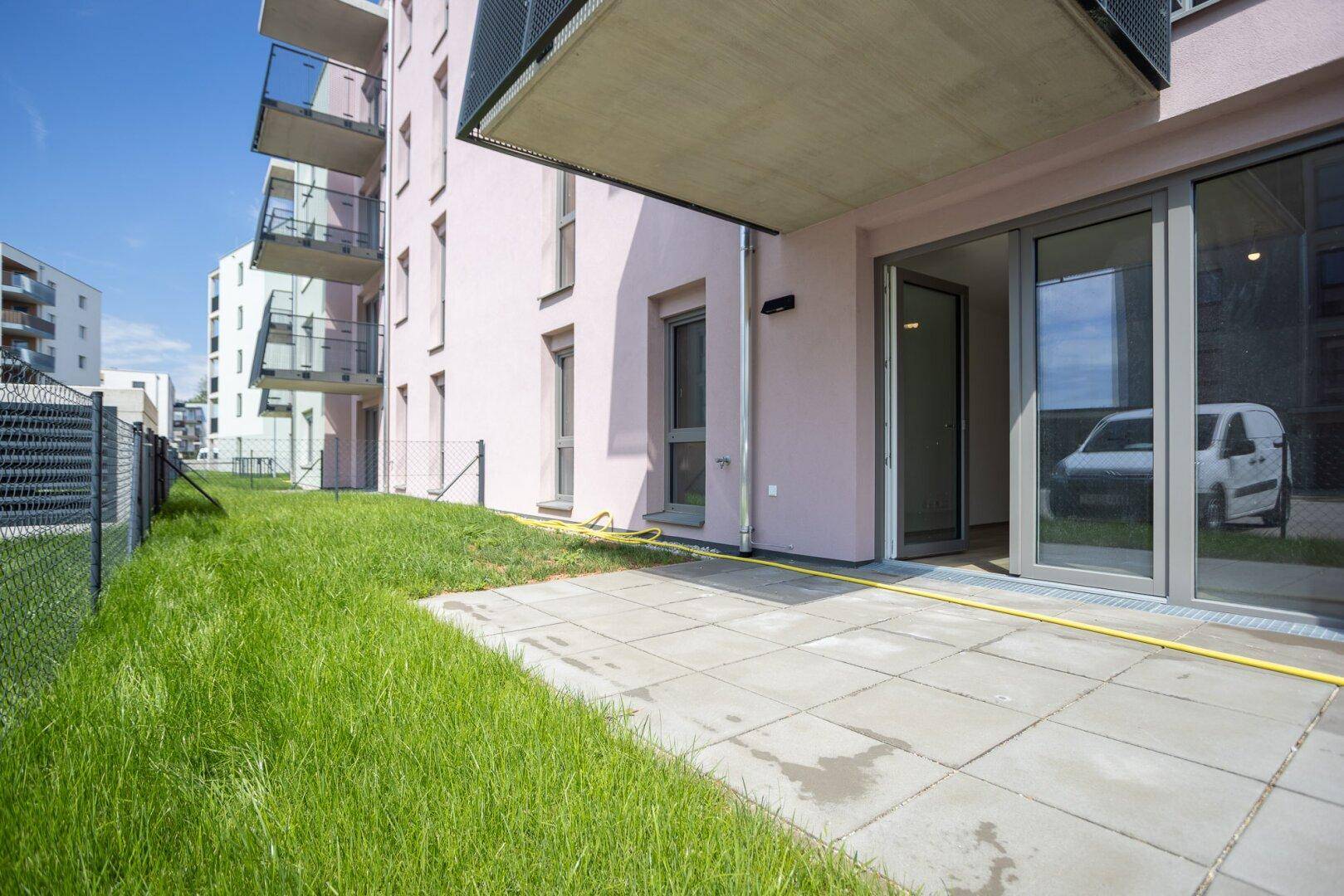 Erdgeschosswohnung mit kleiner gepflasterter Terrasse und angrenzender Rasenfläche.