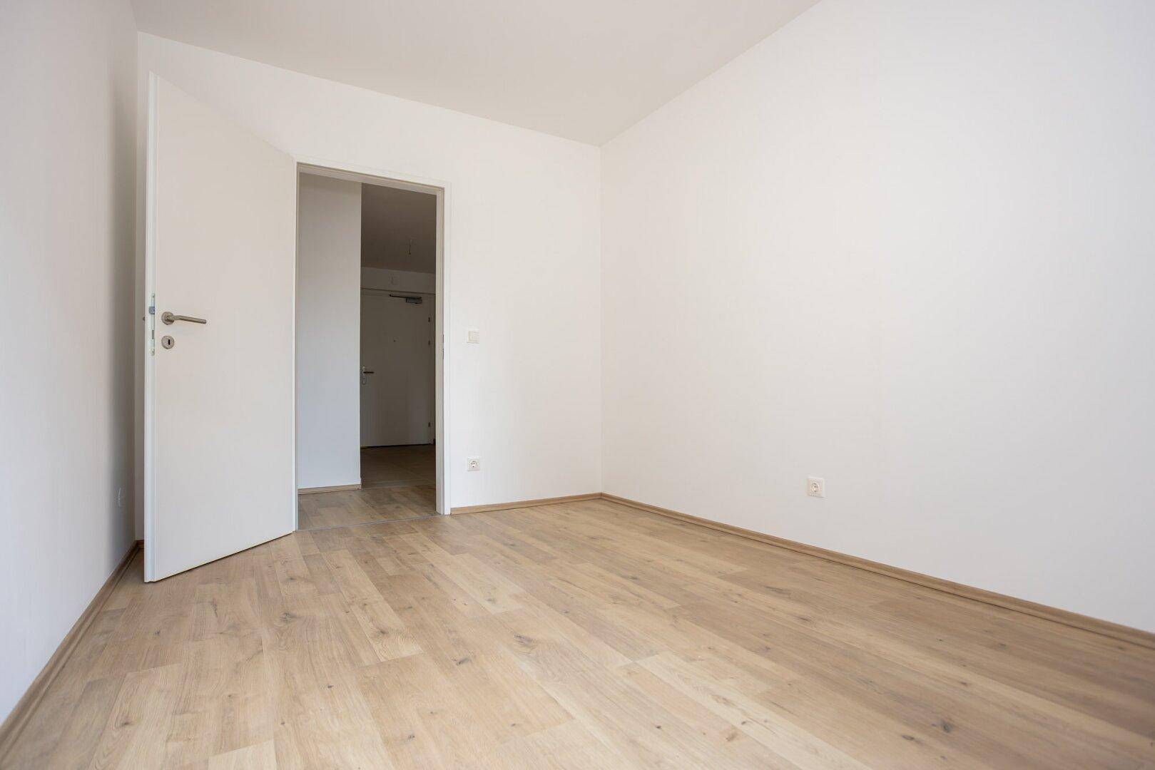 Leeres Schlafzimmer mit hellem Laminatboden und weiß gestrichenen Wänden.