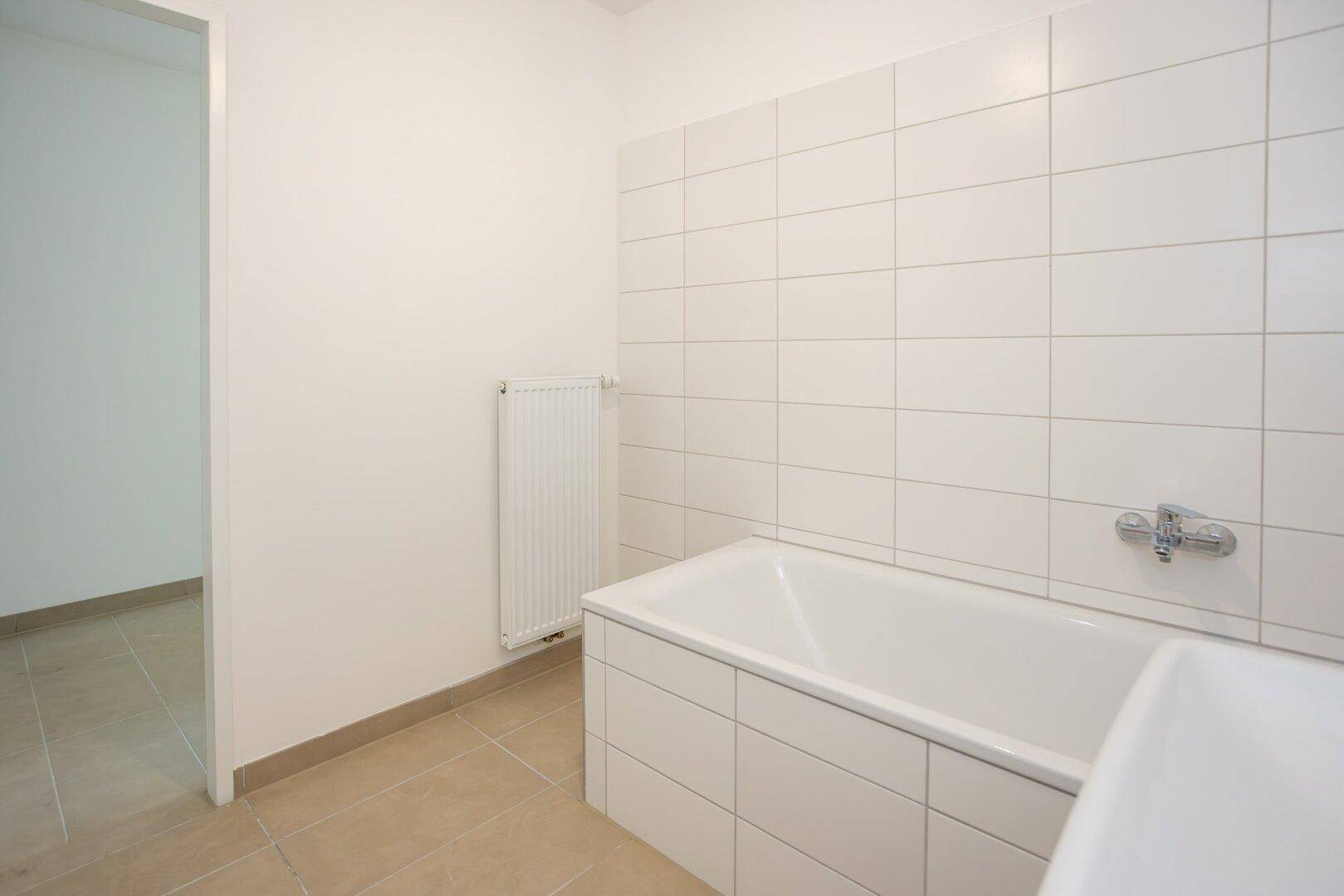 Badezimmer mit weiß gefliesten Wänden, Badewanne und Heizkörper.