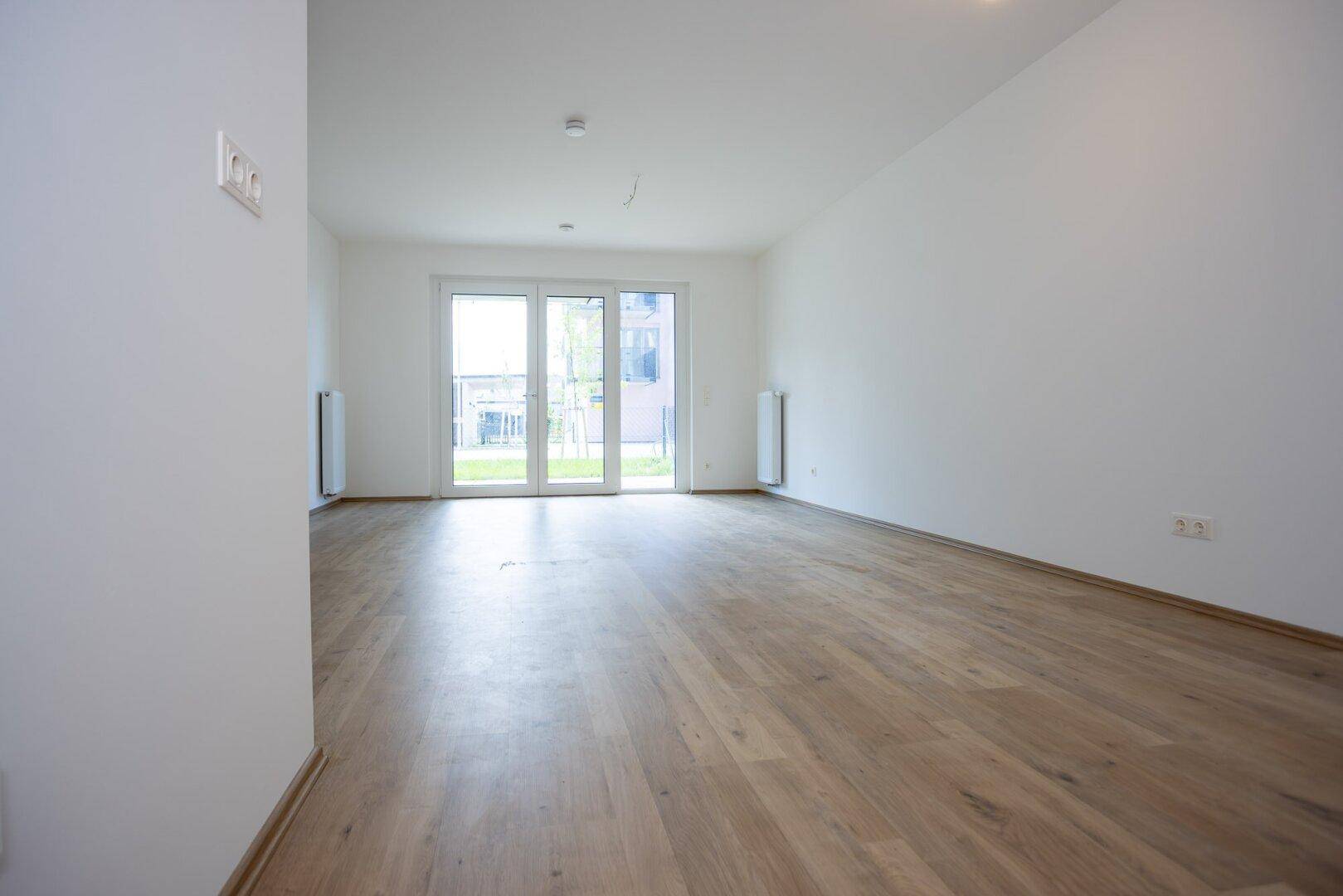 Geräumiges Wohnzimmer mit hellem Laminatboden und großer Terrassentür.