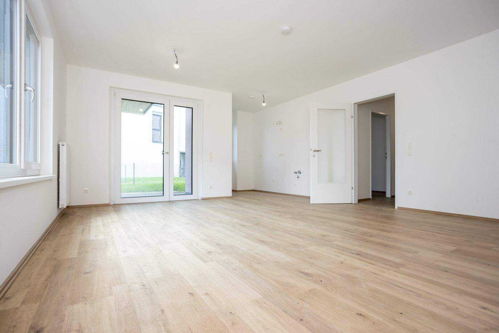 Heller Wohnbereich mit Laminatboden, Zugang zum Garten und einer Tür zu weiteren Räumen.