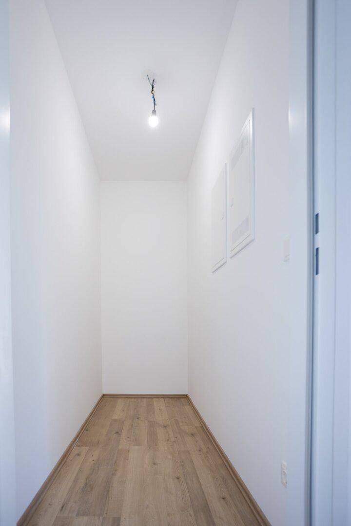 Schmaler, heller Flur mit weißen Wänden und durchgehendem Laminatboden.