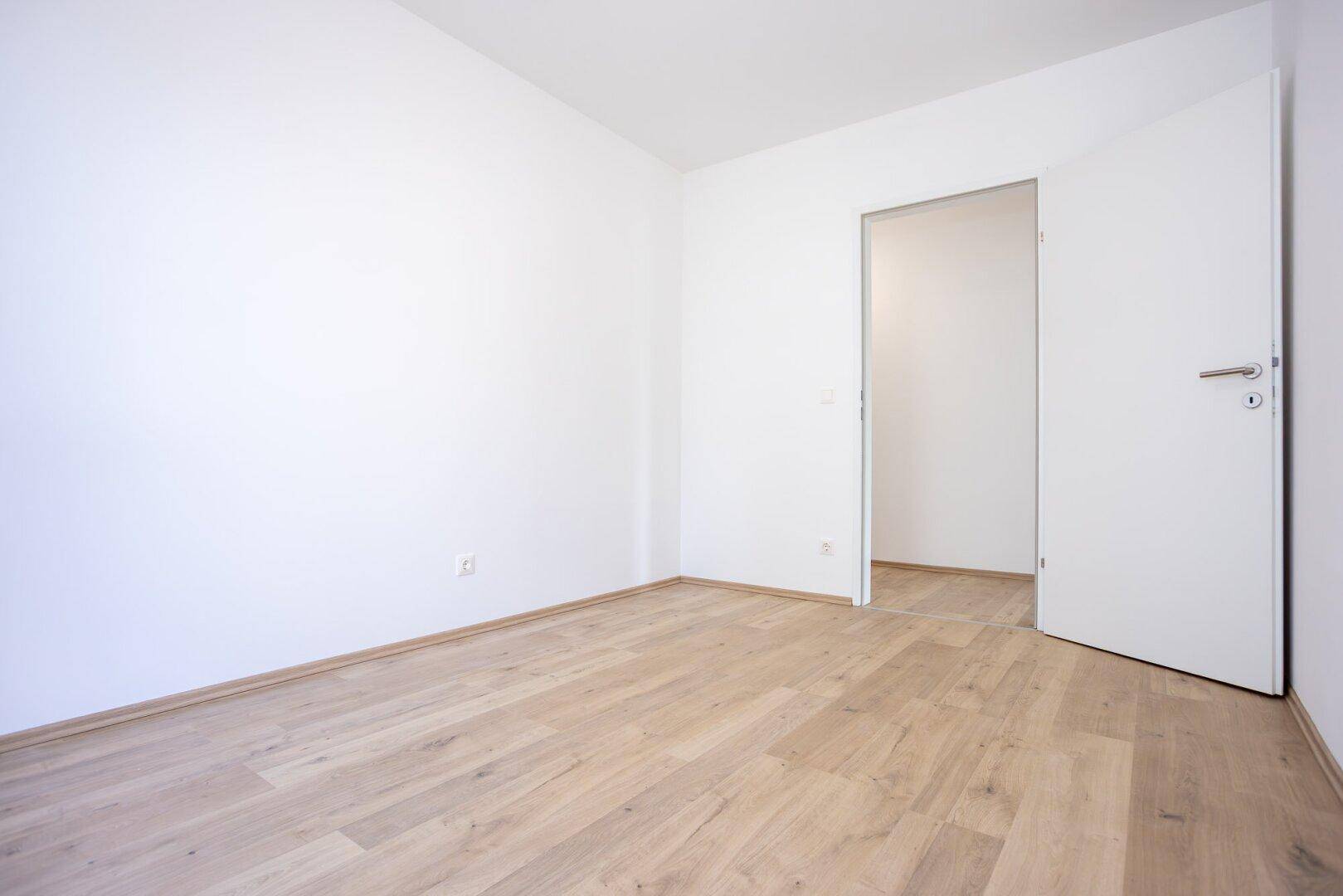 Leeres Zimmer mit weißen Wänden und hellem Laminatboden, bereit zur individuellen Gestaltung.
