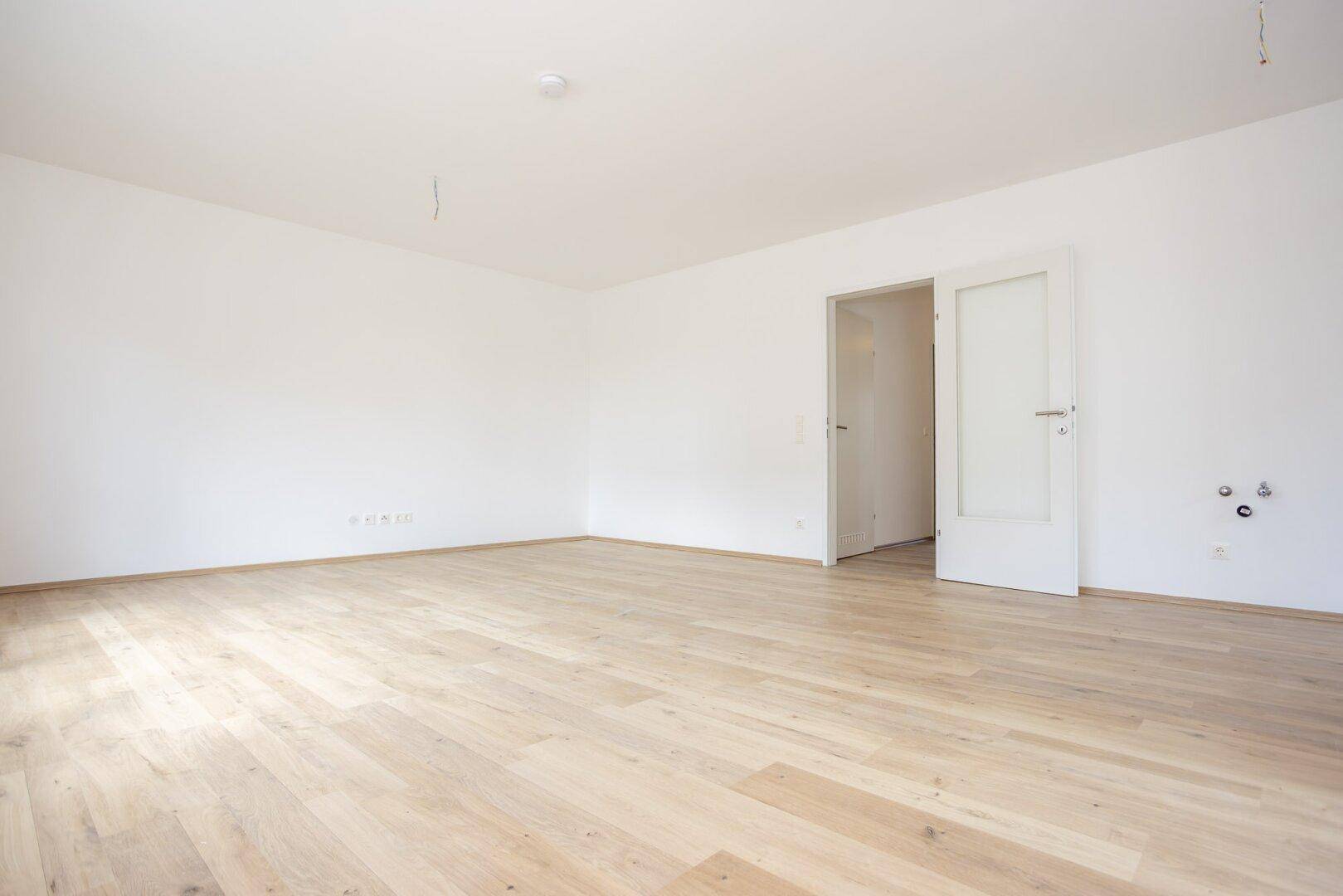 Leerer Wohnraum mit hellem Laminatboden und weißen Wänden, bereit für die individuelle Gestaltung.