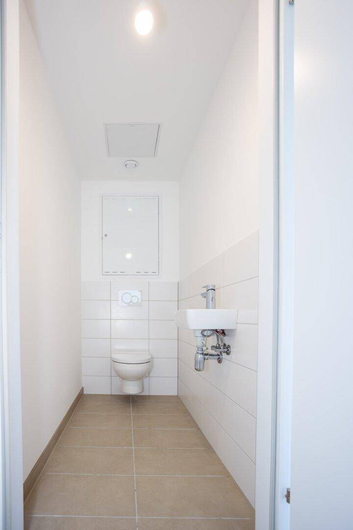 Modernes Gäste-WC mit wandhängender Toilette, kleinem Waschbecken und hellen Fliesen.