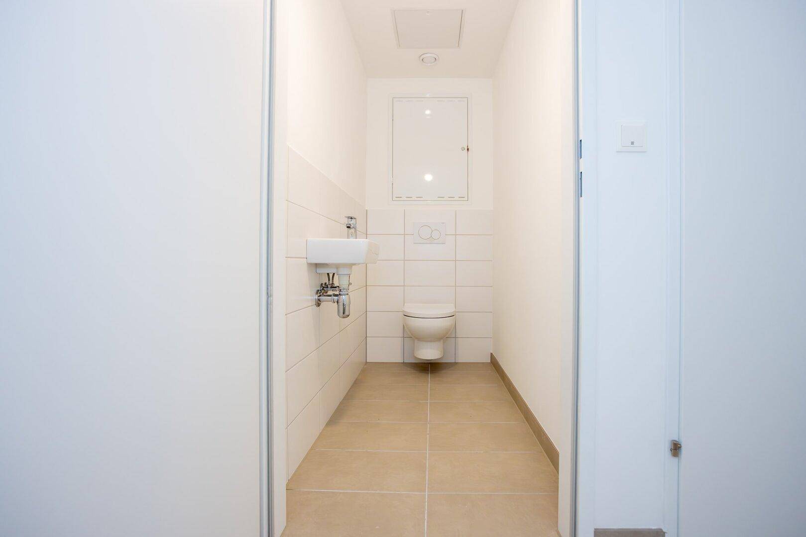Modernes Gäste-WC mit wandhängendem WC, kleinem Waschbecken und hellen Fliesen.