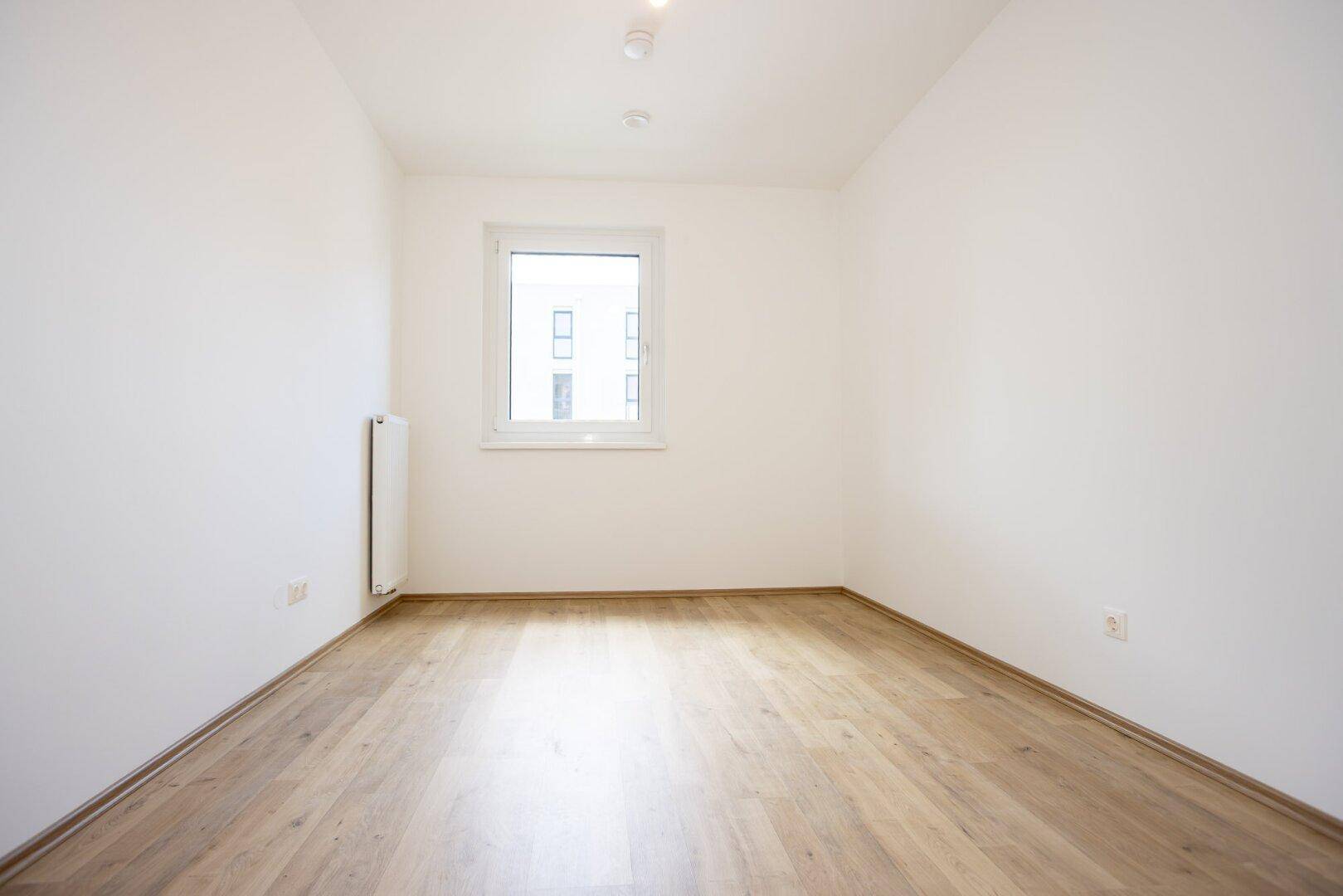 Helles Zimmer mit Laminatboden, weißen Wänden und einem Fenster, ideal als Schlafzimmer.
