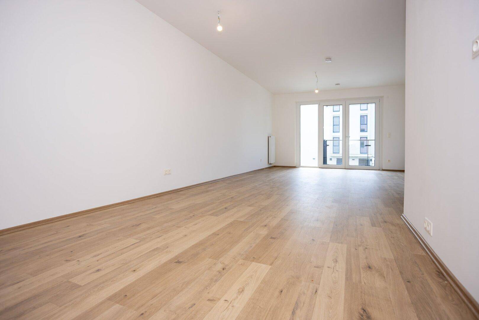 Großes Wohnzimmer mit hellem Laminatboden und breiter Schiebetür, die zu einem Außenbereich führt.