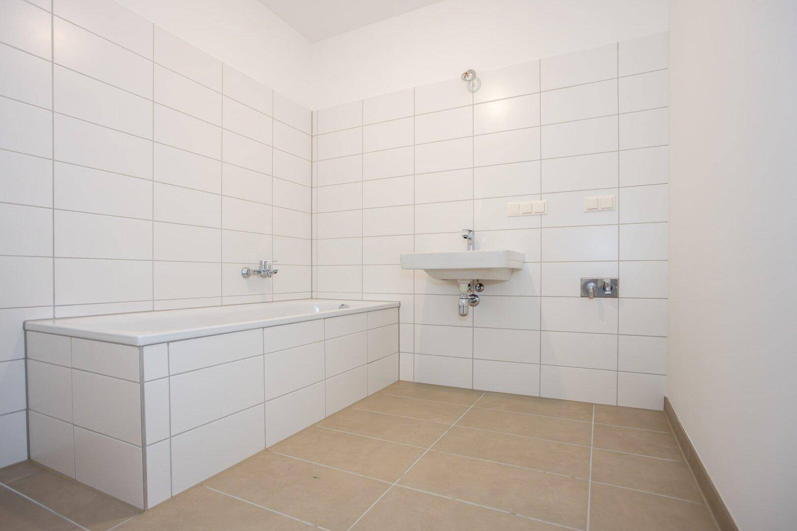 Helles Badezimmer mit Badewanne und Waschbecken, komplett gefliest in neutralen Farben, sehr gepflegt.