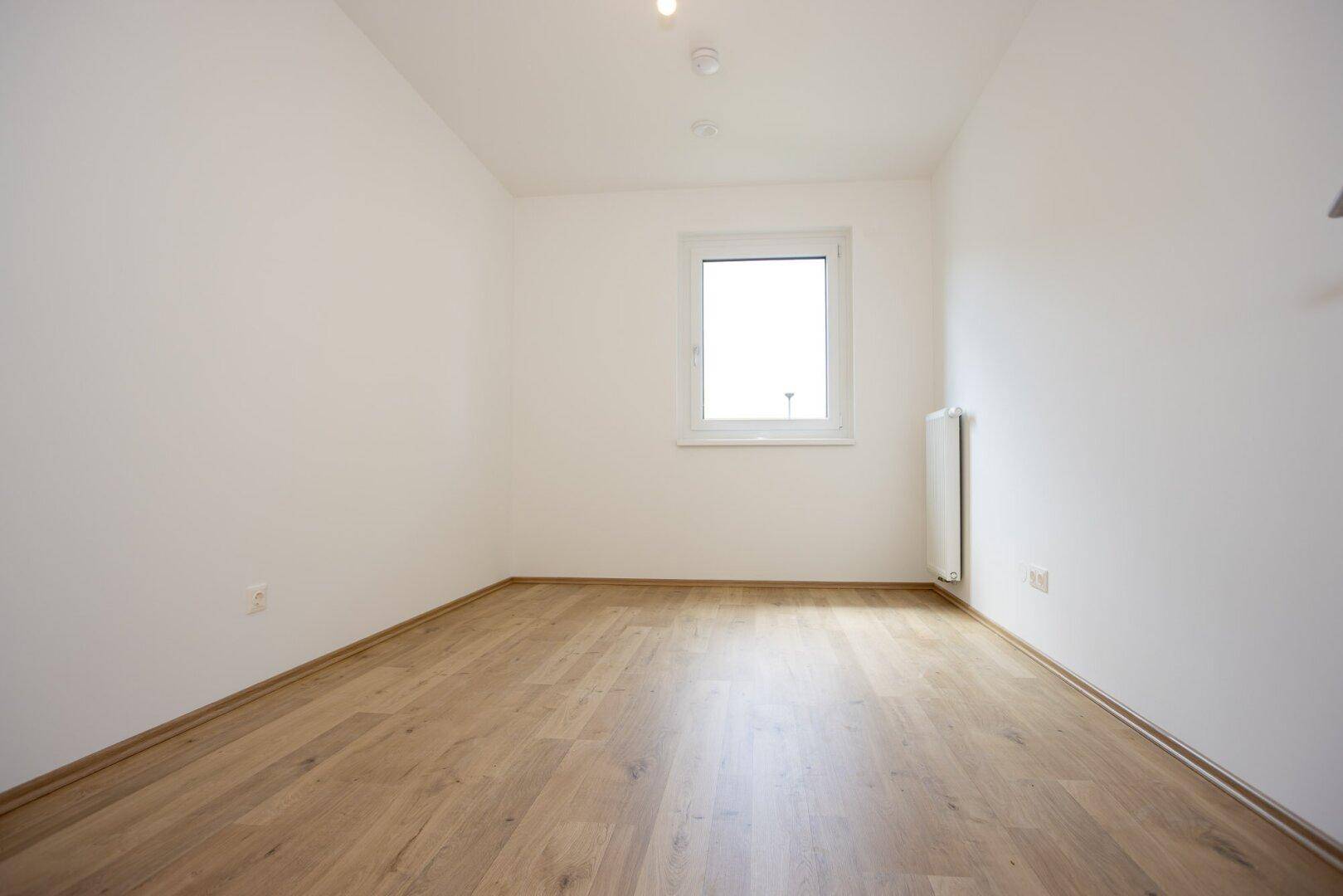 Leeres Zimmer mit Laminatboden und einem Fenster, ideal als Schlaf- oder Arbeitszimmer, sehr hell.