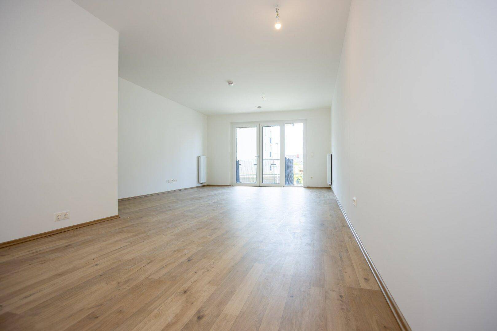 Geräumiges Wohnzimmer mit Laminatboden und Zugang zu einem Balkon, hell und modern gestaltet.