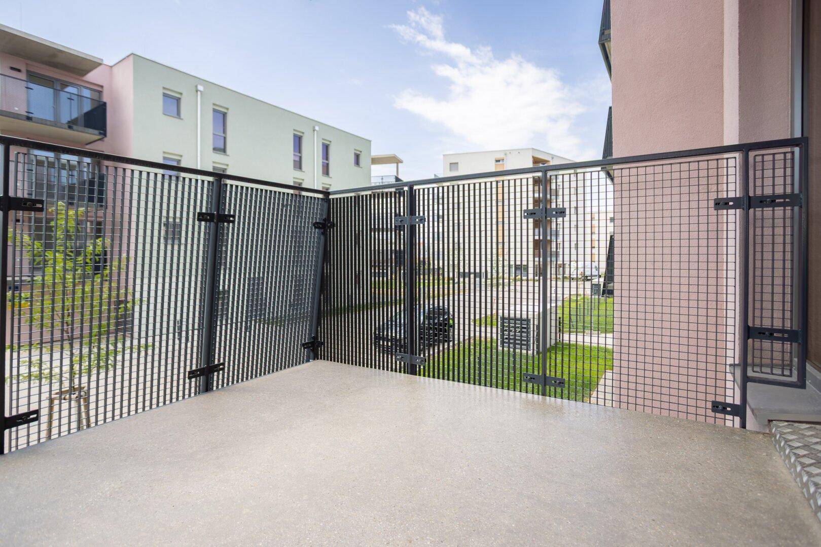 Kleine Terrasse im Erdgeschoss mit Metallzaun und Blick auf die moderne Wohnanlage.