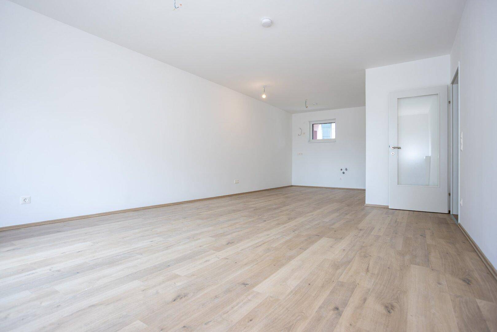 Leeres Zimmer mit hellem Laminatboden und einem Fenster, bereit zur individuellen Gestaltung.
