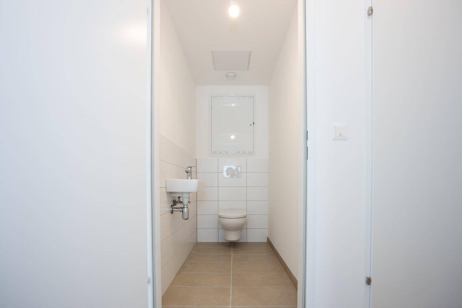 Modernes Gäste-WC mit weiß gefliesten Wänden und kleinem Waschbecken.