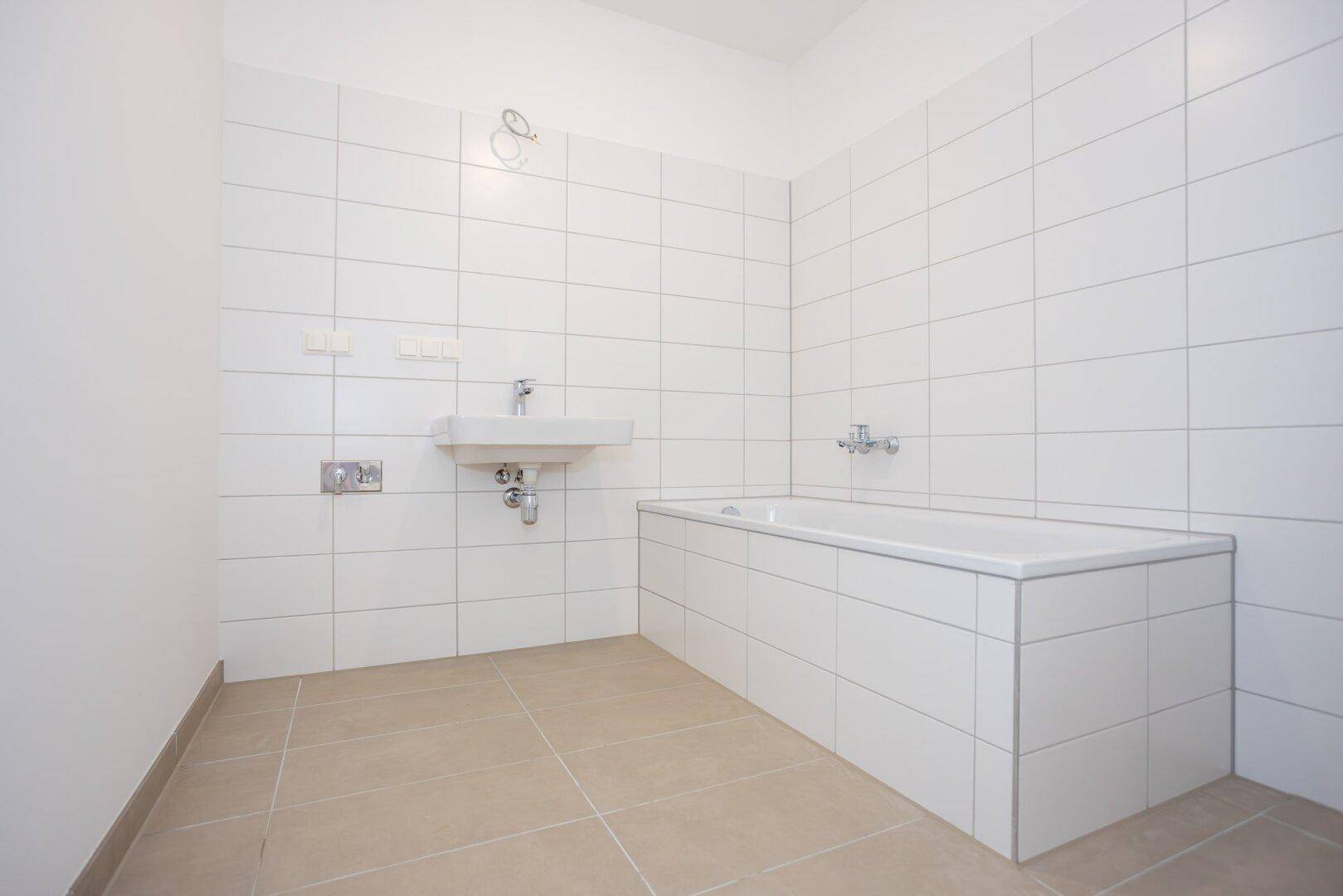 Geräumiges Badezimmer mit weißer Badewanne, Waschbecken und hellen Fliesen.