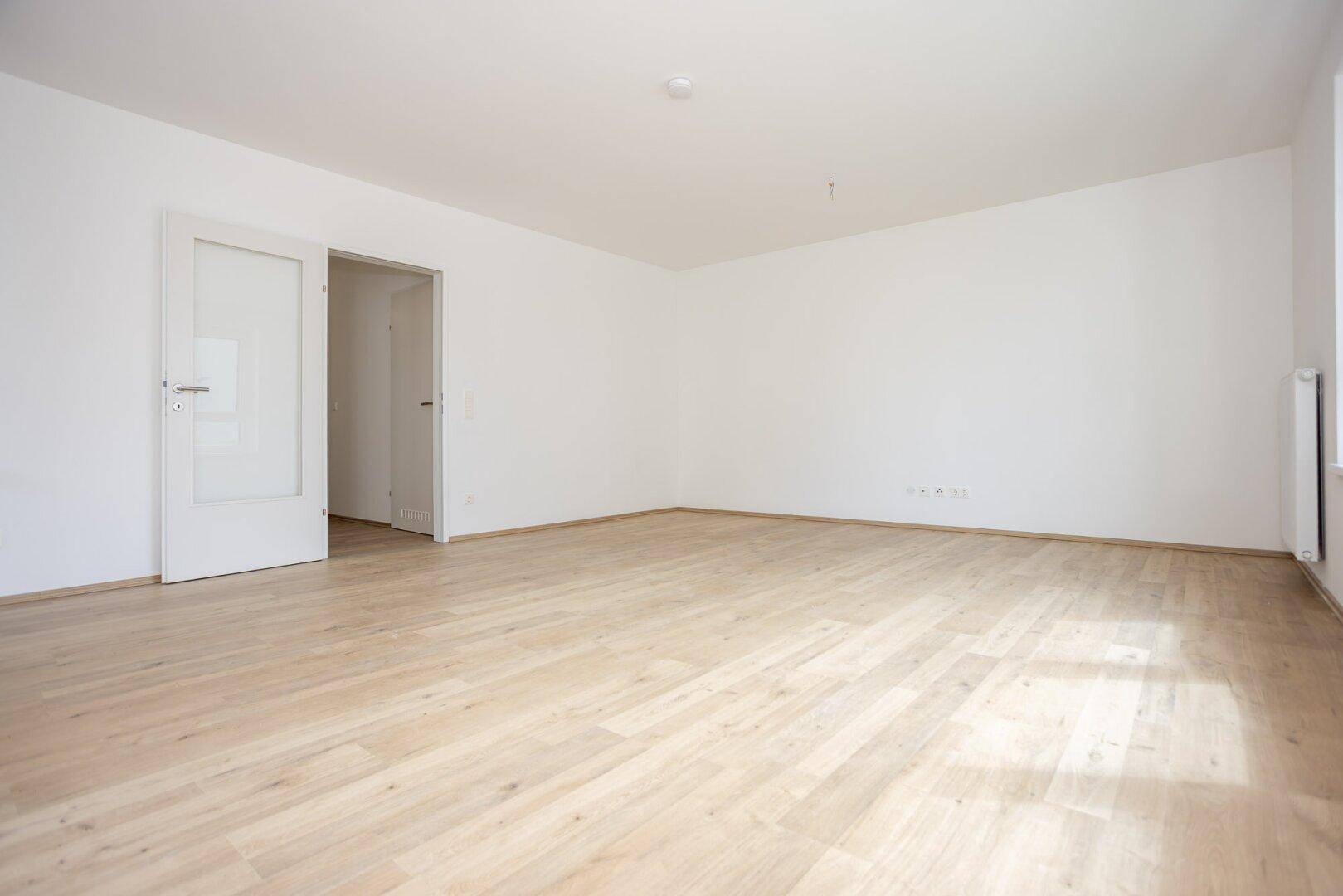 Heller Wohnbereich mit Laminatboden und weiß gestrichenen Wänden, bereit zur individuellen Gestaltung.