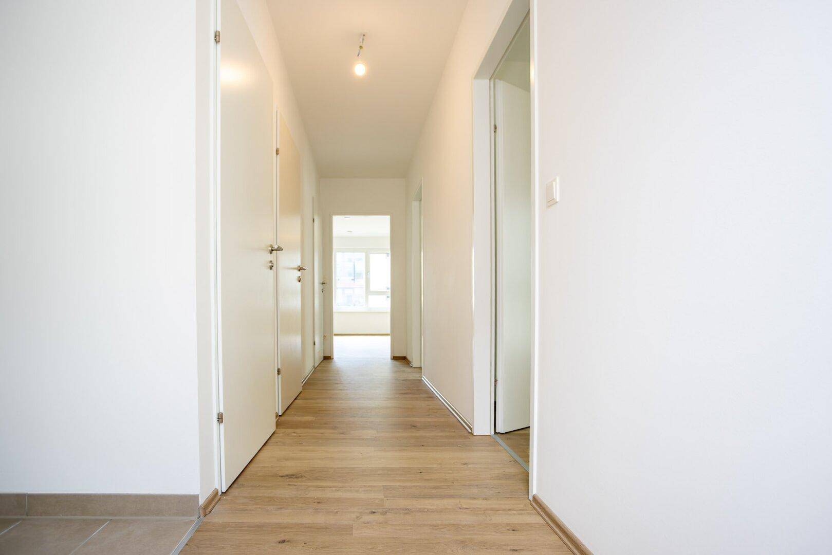 Langer, heller Flur mit Laminatboden und mehreren Türen zu den angrenzenden Räumen.