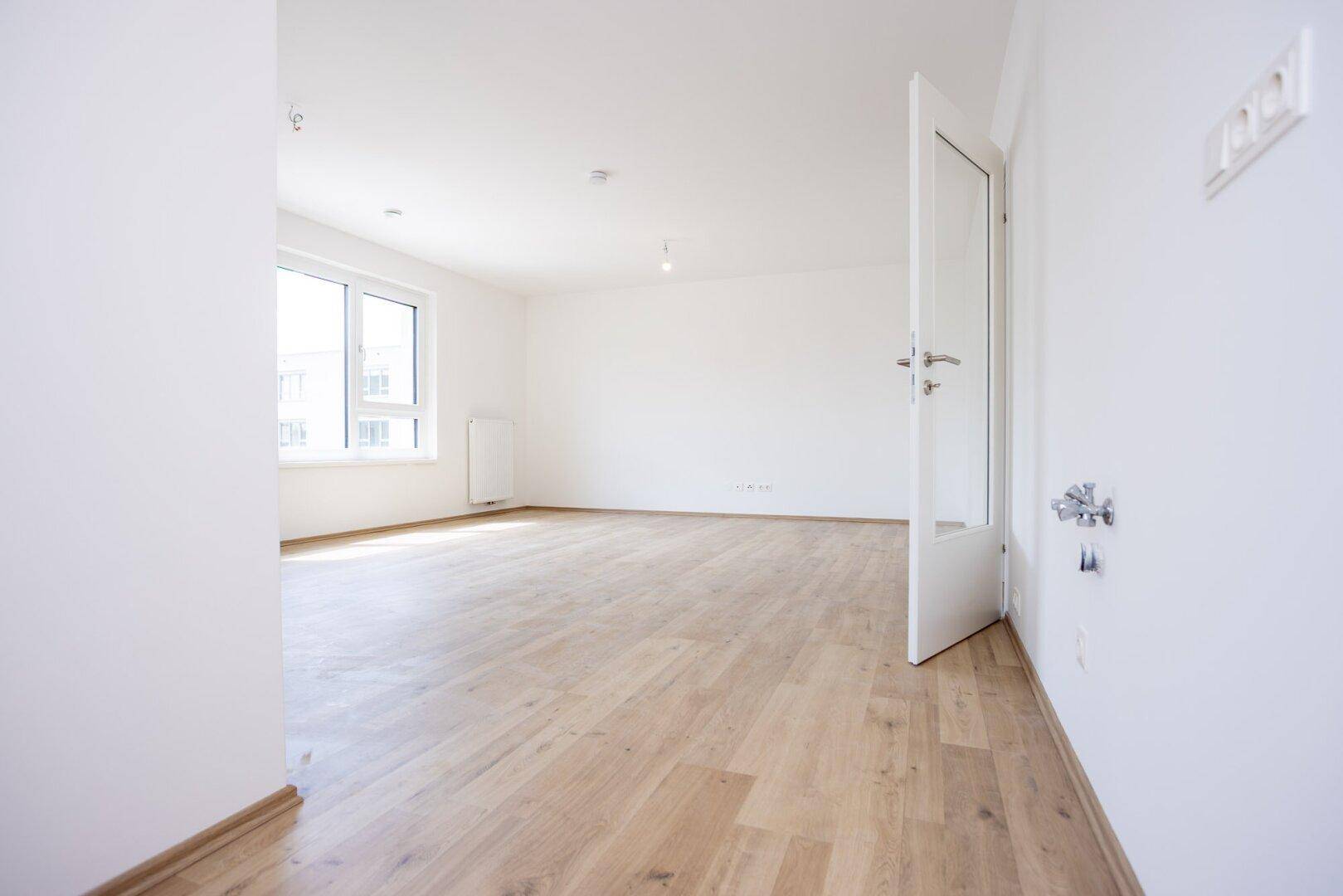 Heller Innenraum mit Laminatboden und einem Fenster, möglicherweise für eine Küche oder einen Flur vorgesehen.