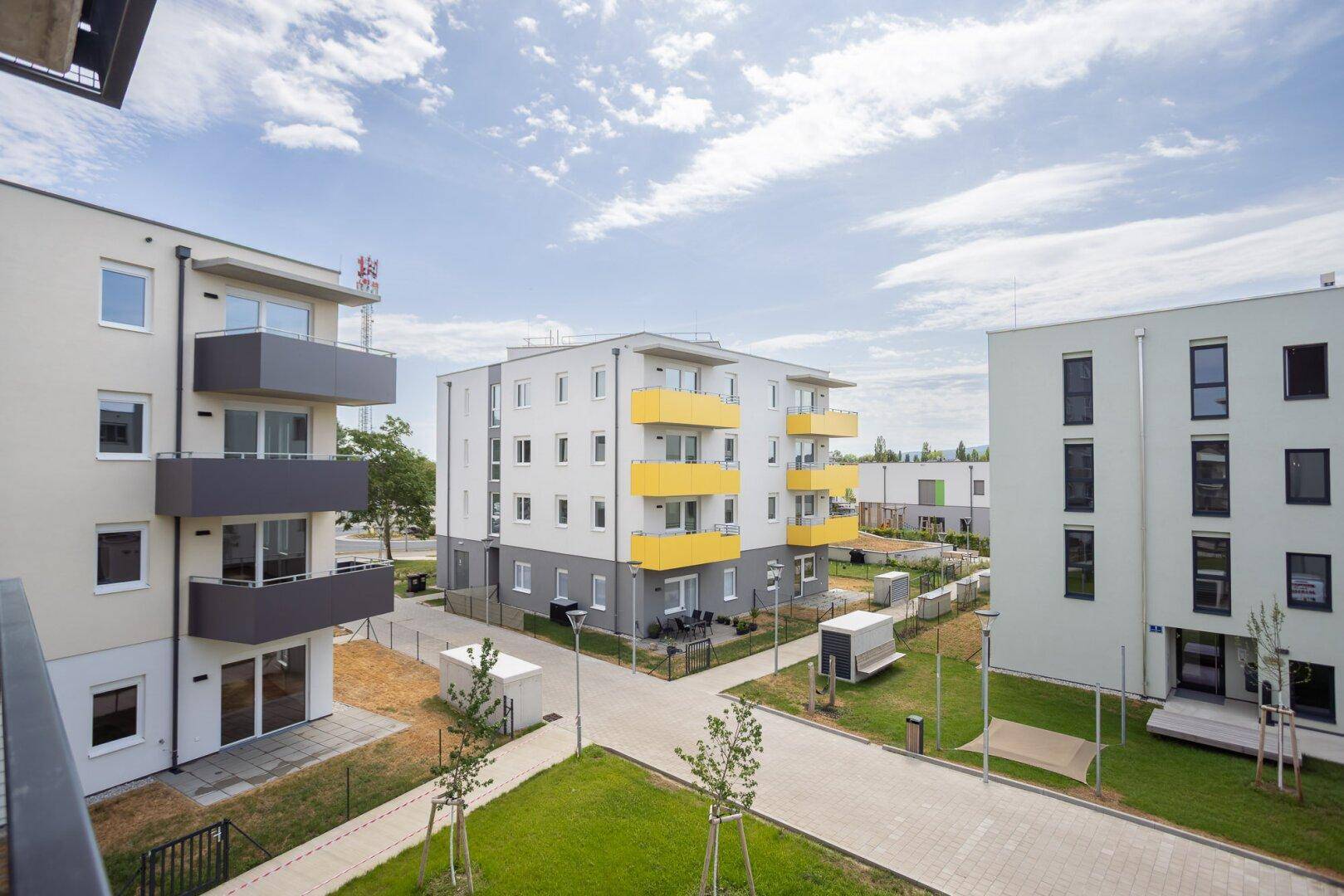 Moderne Wohngebäude mit farbigen Balkonen und gepflegten Grünflächen in einer neuen Wohnsiedlung.