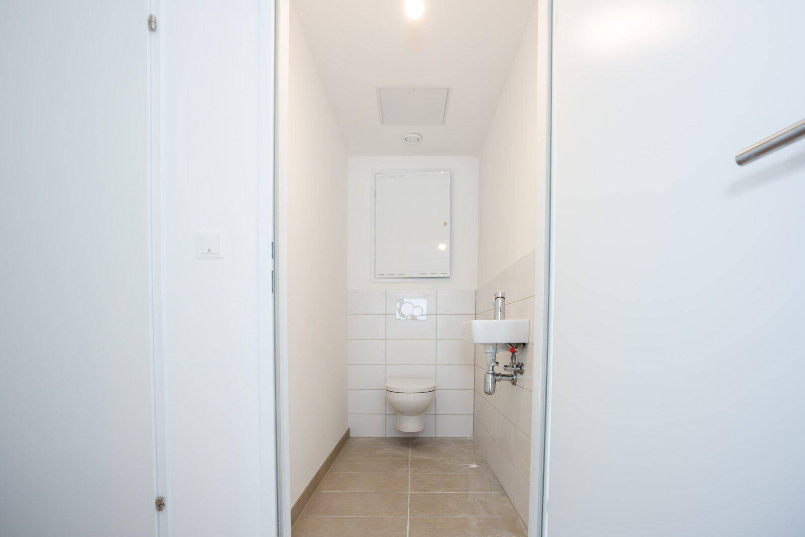 Kleines Gäste-WC mit weißen Fliesen, einer Toilette und einem kompakten Waschbecken.