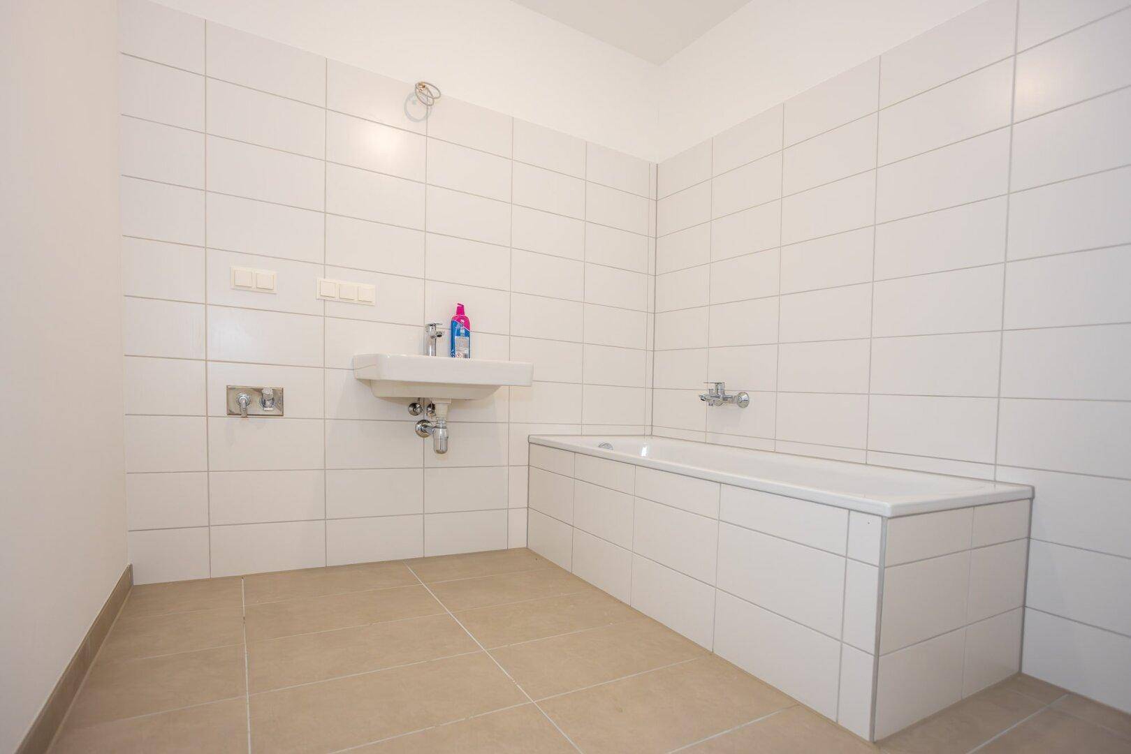 Modernes Badezimmer mit Badewanne, Waschbecken und weißen Wandfliesen, bereit zur individuellen Gestaltung.