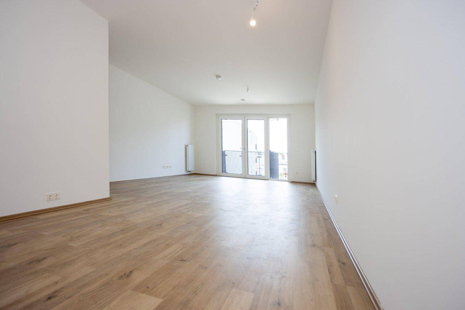 Geräumiger, heller Raum mit Laminatboden und Zugang zu einem Balkon.