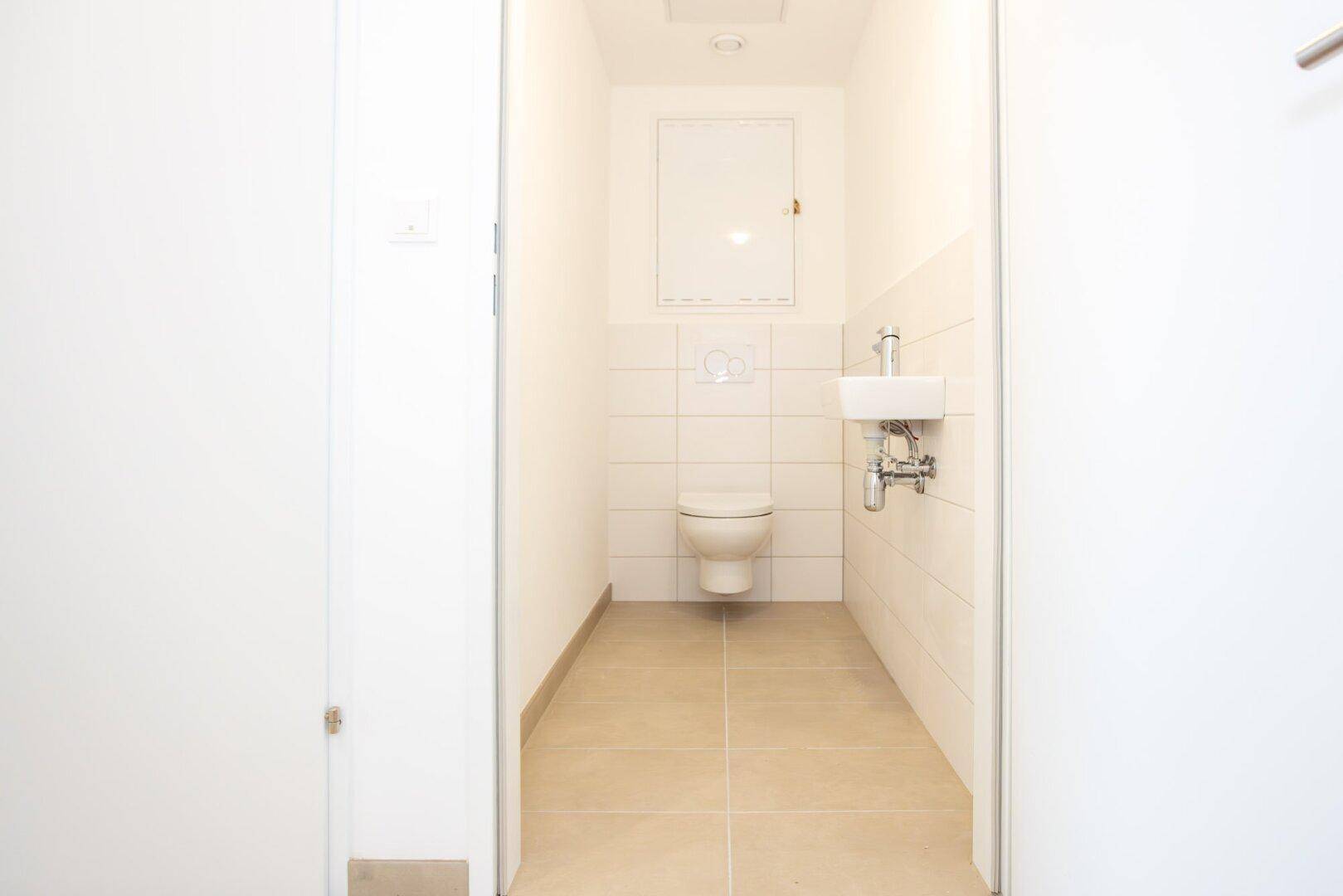 Modernes Gäste-WC mit wandhängendem WC, kleinem Waschbecken und hellen Fliesen.