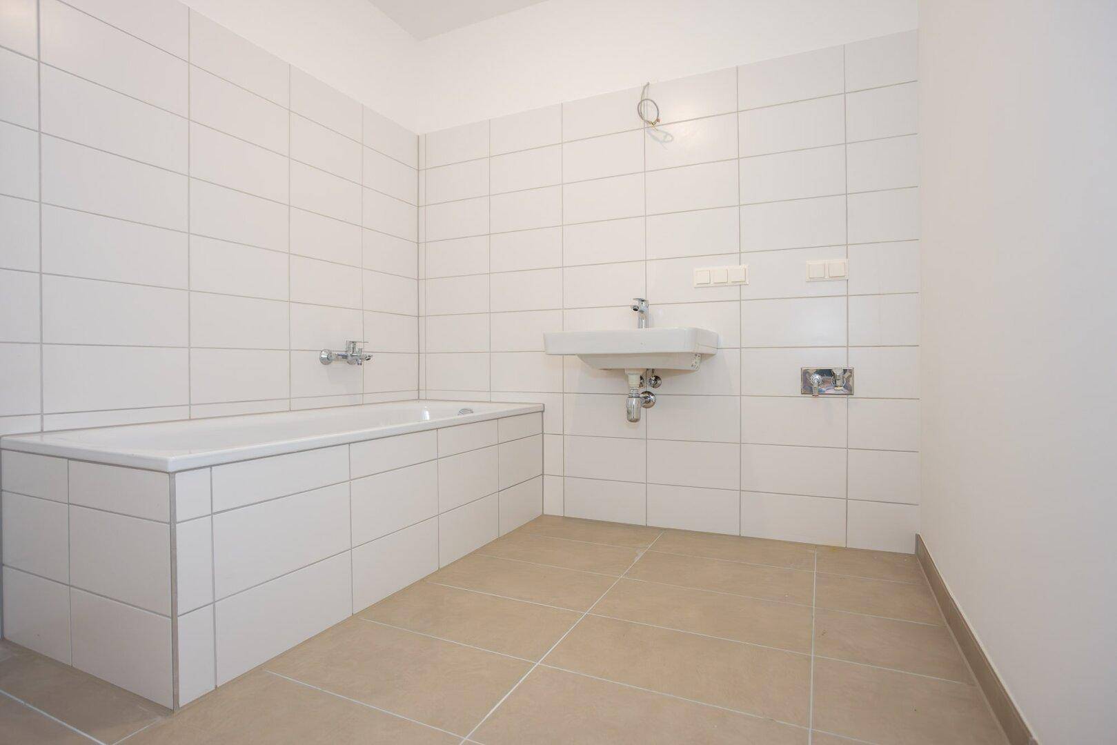 Badezimmer mit weiß gefliesten Wänden, eingebauter Badewanne und einem Waschbecken.
